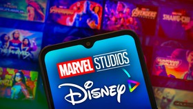 Marvel Studios and Disney Plus logos on phone with MCU banner posters in background